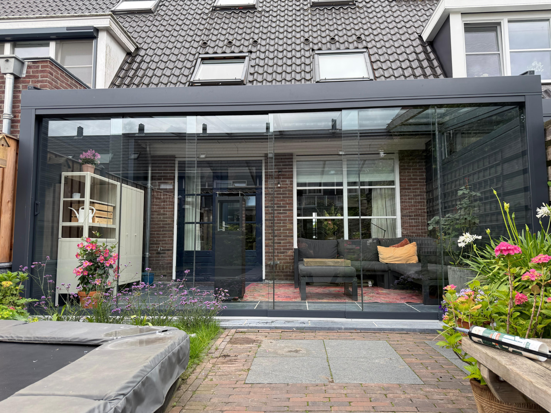 Moderne aluminium veranda met glazen schuifwanden en glazen dak, geïntegreerd in een karakteristieke Nederlandse woning